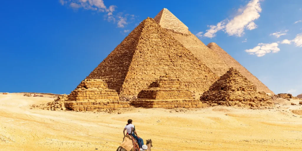 Camel ride in front of the Great Pyramids of Giza, Egypt. Desert landscape, blue sky.